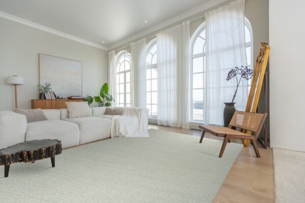 Light green textured rug grounds a living room with a white sectional, wood chair, and large arched windows.