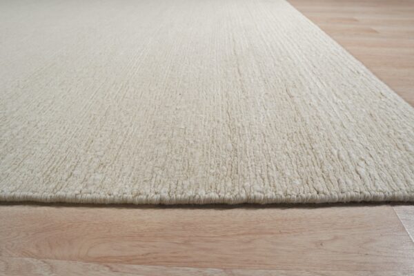 Detailed view of a thick, textured, solid off-white rug next to light wood planks.