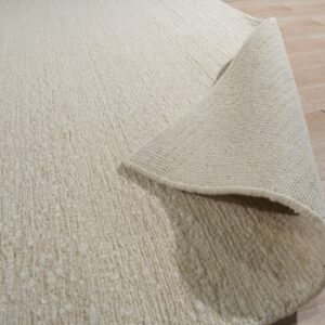 A textured ivory rug is curled back, showing the backing and light wood flooring.