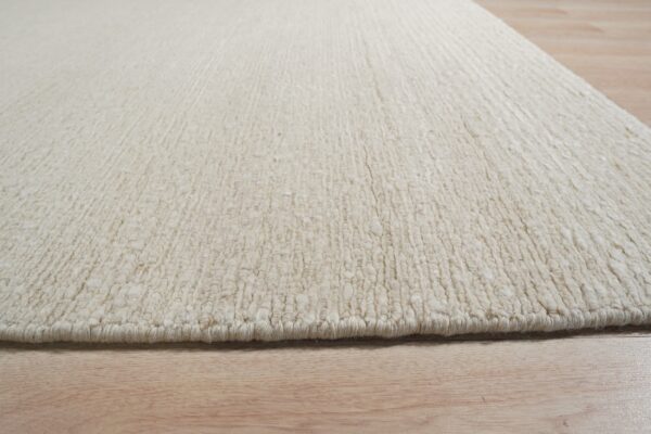 Textured off-white rug with thick vertical ribs resting on light natural wood planks.