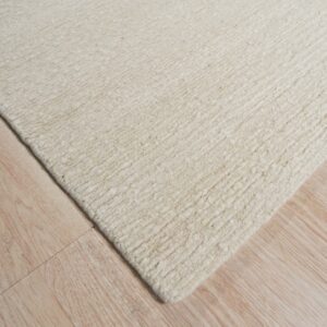 Textured cream rug with chunky horizontal rows rests diagonally on light blonde wood planks.