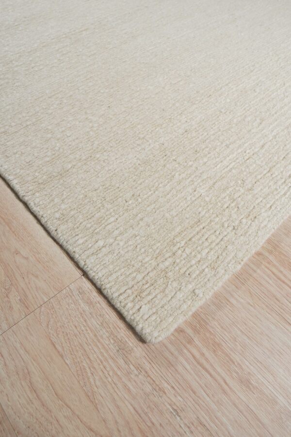 Textured cream rug with chunky horizontal rows rests diagonally on light blonde wood planks.