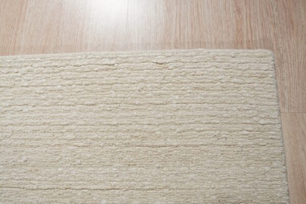 A textured light beige rug with thick horizontal loops lies on pale, reflective wood flooring.