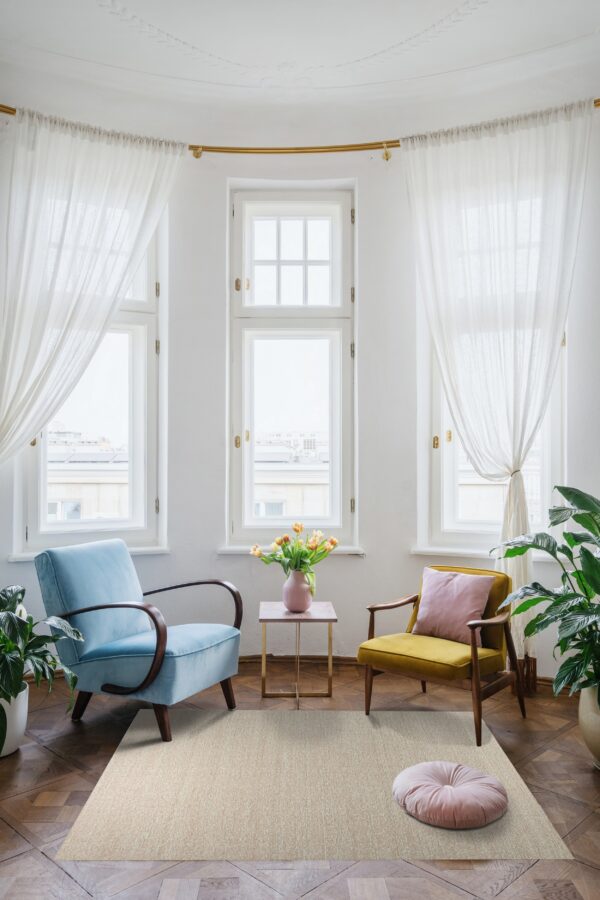 A speckled light beige rug anchors a bright bay window seating area with two colorful velvet chairs and wood floors.