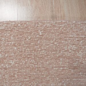 Textured pale pink rug with chunky off-white knots rests on a light blonde wooden floor.