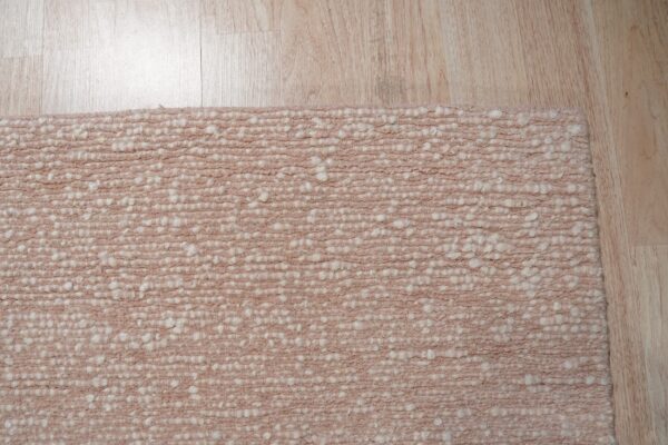 Textured pale pink rug with chunky off-white knots rests on a light blonde wooden floor.
