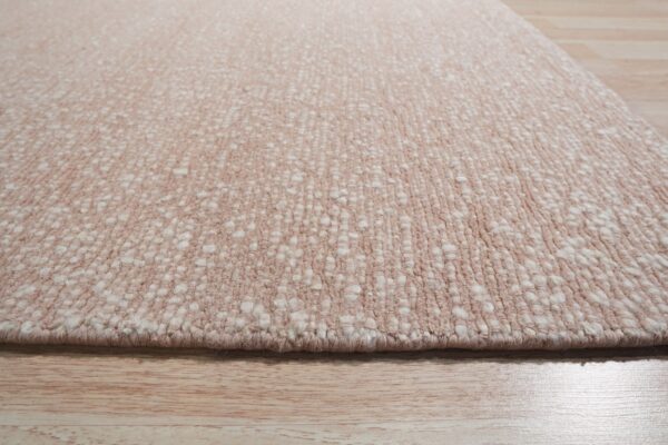 Angled view of a blush pink rug featuring a dense, nubby texture resting on light natural wood floors.
