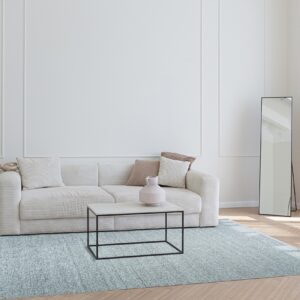 A rectangular speckled blue rug grounds a light-filled room featuring a cream sofa and herringbone wood floor.