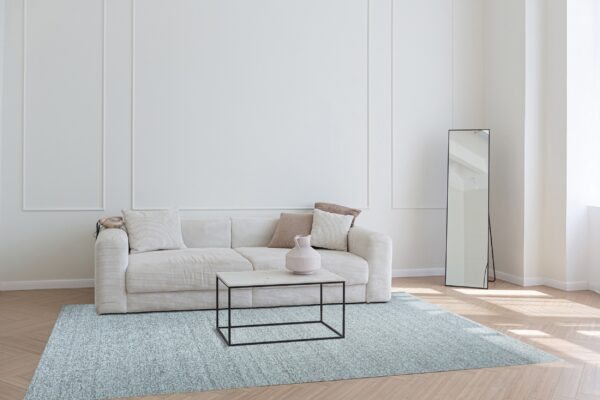 A rectangular speckled blue rug grounds a light-filled room featuring a cream sofa and herringbone wood floor.