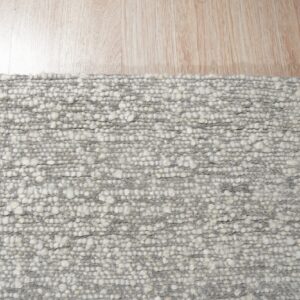 Chunky gray and white textured rug detail resting on light natural wood plank flooring.