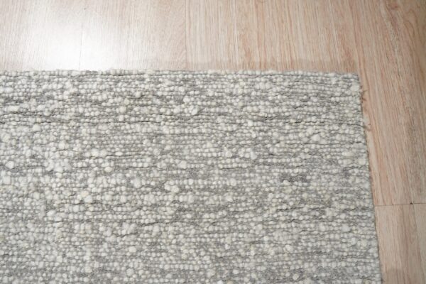 Chunky gray and white textured rug detail resting on light natural wood plank flooring.