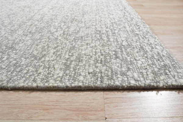 Textured gray and white rug with chunky pile shown from a low angle on light wood flooring.