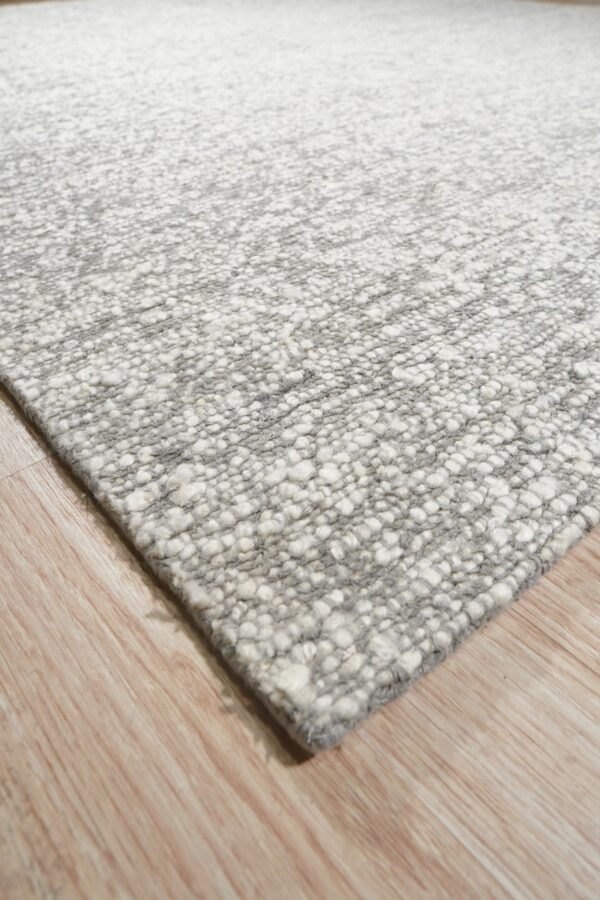 Mottled gray and white rug with a chunky, textured surface rests on light wood flooring.