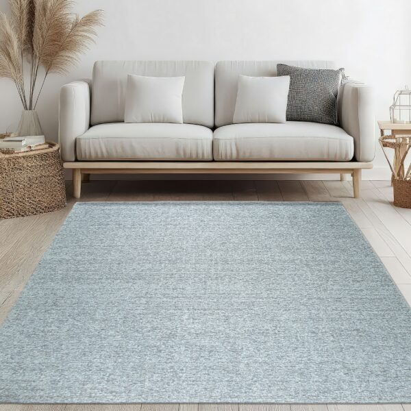 A pale blue textured rug sits under a cream sofa with a wooden base on light plank flooring.