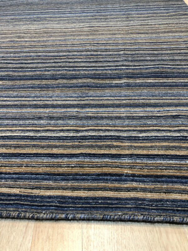 A ribbed rug with horizontal stripes in shades of blue, tan, and gray on light wood flooring.