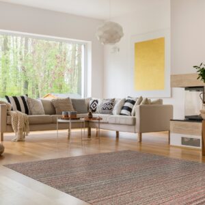 Rust and grey striped low-pile rug placed beneath a beige sectional sofa on polished wood floors.