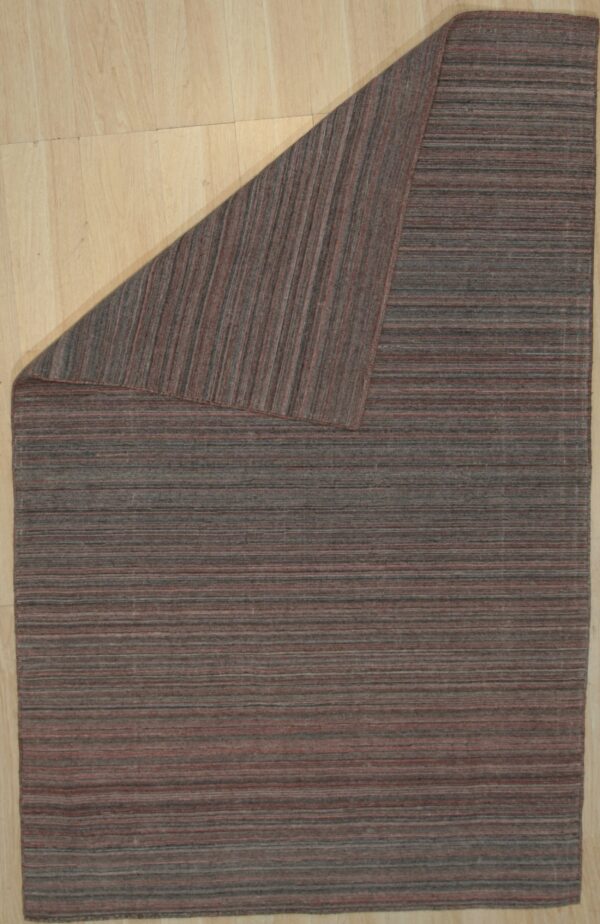 Low-pile rug with horizontal variegated gray and reddish-brown stripes, folded on light wood.