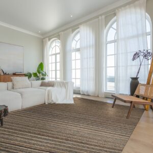 A striated brown and black area rug grounds a bright living room with a white sectional and arched windows.