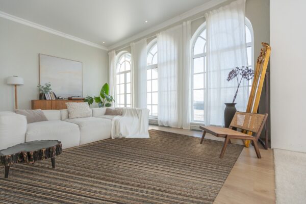 A striated brown and black area rug grounds a bright living room with a white sectional and arched windows.