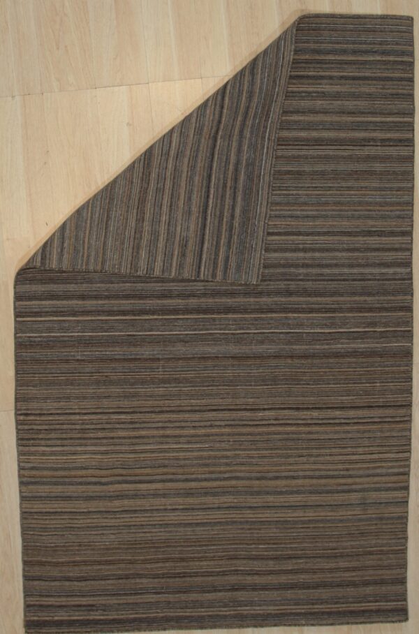Brown and tan striped rug on a light wood floor with the upper corner folded back.