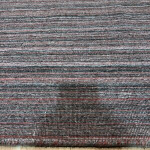 Textured low-pile rug with horizontal bands of charcoal gray, rust, and light blue on light wood flooring.
