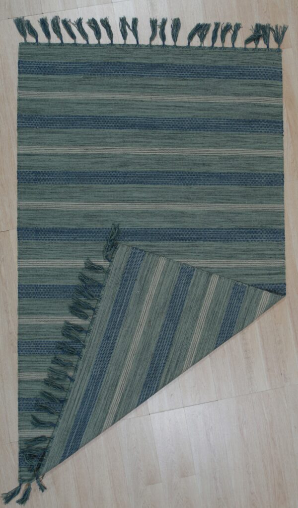 Teal and navy striped low-pile rug with tassels, folded over to show vertical stripes on the reversible side.