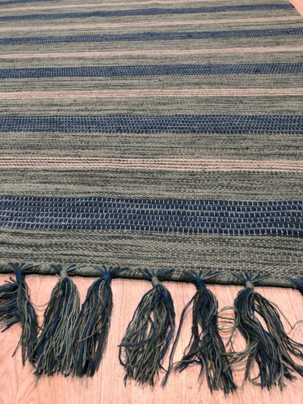 Striped flatweave rug featuring textured blue and gray bands, finished with knotted blue and green tassels.