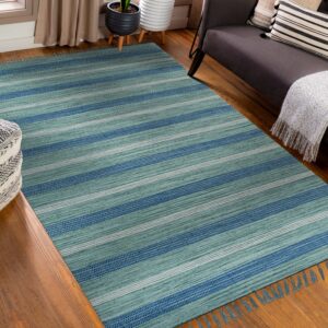 Teal and blue striped flatweave rug displayed on wood flooring next to a dark sofa and ottoman.