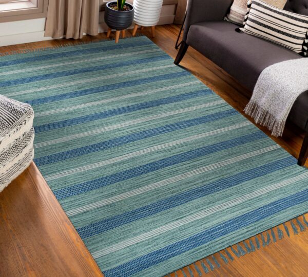 Teal and blue striped flatweave rug displayed on wood flooring next to a dark sofa and ottoman.
