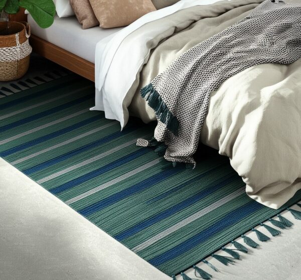Teal, blue, and gray striped rug with tassels on light gray flooring near a bed.