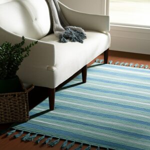 A striped blue, green, and white flatweave rug with fringe lies beneath a cream upholstered chair on a wood floor.