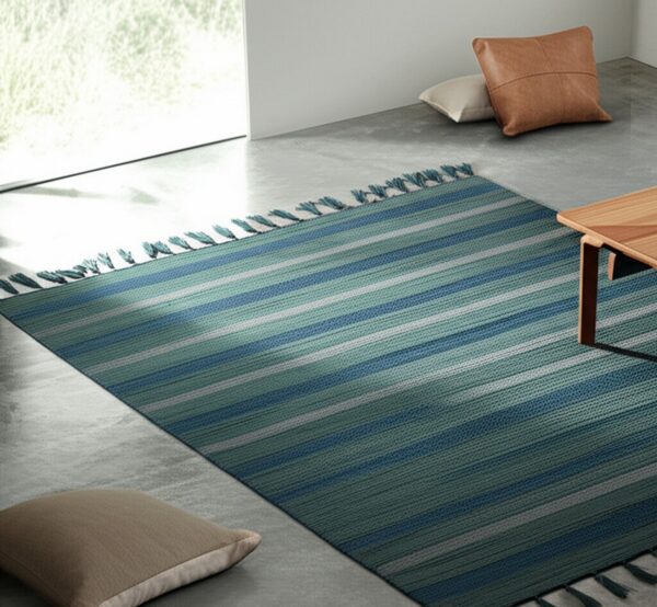 Woven low-pile rug featuring blue, teal, and white stripes sits on a gray floor near a window and wooden table.