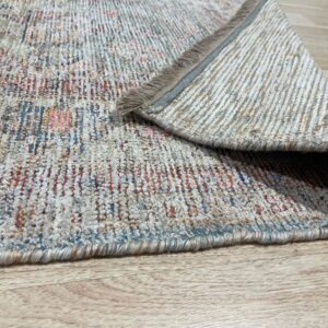 Multicolor textured rug, featuring blue, rust, and cream colors, folded over on light wood flooring.