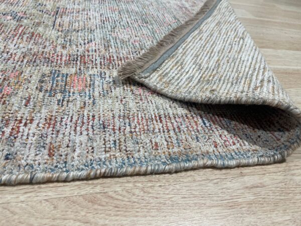 Multicolor textured rug, featuring blue, rust, and cream colors, folded over on light wood flooring.