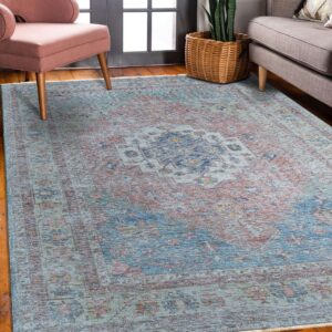 A distressed traditional rug in faded teal, rust, and navy rests on hardwood floors near upholstered seating.