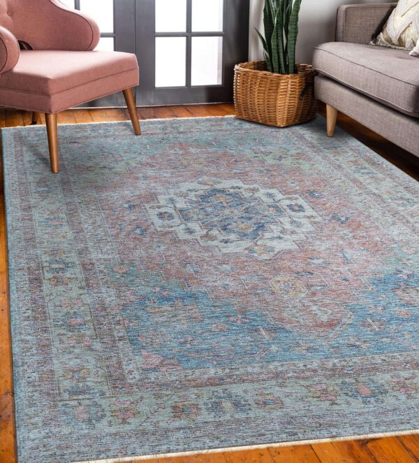 A distressed traditional rug in faded teal, rust, and navy rests on hardwood floors near upholstered seating.