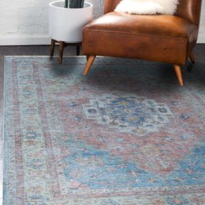 A distressed blue and terracotta medallion rug sits beneath a brown leather armchair on dark wood floor.