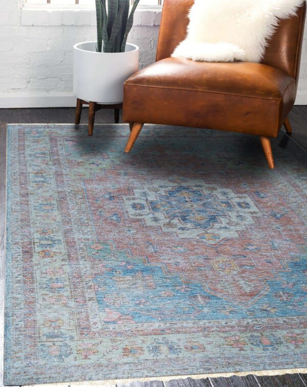 A distressed blue and terracotta medallion rug sits beneath a brown leather armchair on dark wood floor.