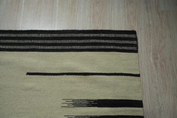 Light beige flatweave rug with thick dark brown stripes and dashed linear patterns on light wood flooring.