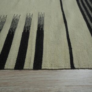 Low-pile rug with cream and dark striped patterns resting on light wood plank flooring.