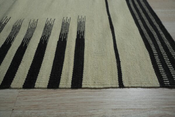 Low-pile rug with cream and dark striped patterns resting on light wood plank flooring.