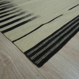 A close-up of a cream and black striped flatweave rug lying on light wood flooring.
