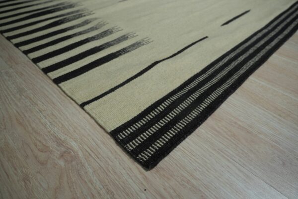 A close-up of a cream and black striped flatweave rug lying on light wood flooring.