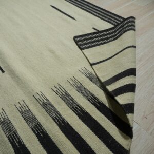 Light-colored flatweave rug with abstract dark stripes and bands displayed on blonde wood flooring.