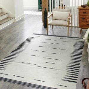Black and white ikat-style rug on gray wood flooring next to a staircase and gold-framed armchair.