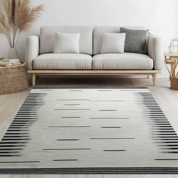 Low pile gray rug with black horizontal dashes and blurred stripes beneath a cream sofa on light wood flooring.