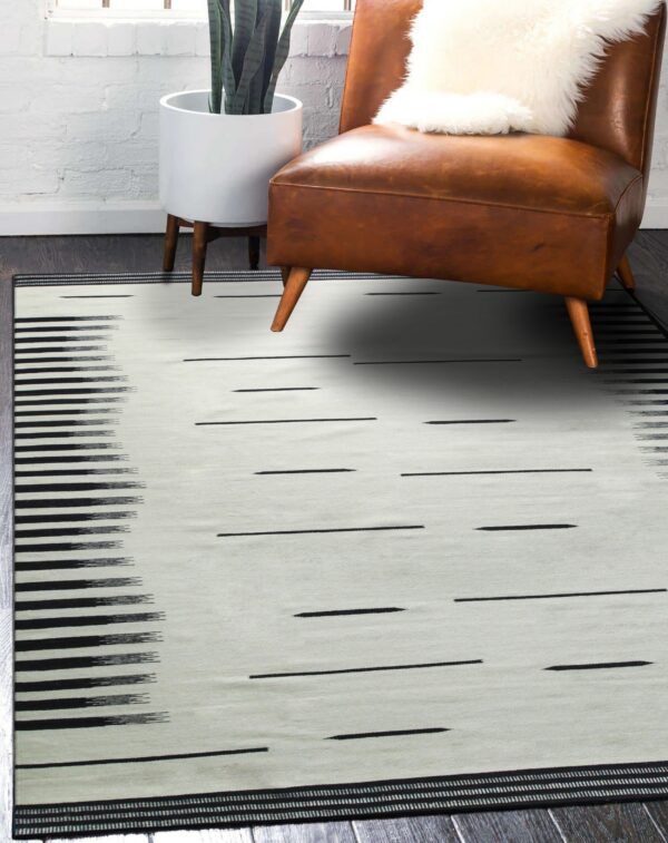 Black and cream flatweave rug with dash patterns and ikat stripes styled with a brown leather chair.
