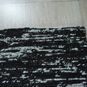Textured black and white rug featuring thick, irregular horizontal striping placed on light wooden flooring.