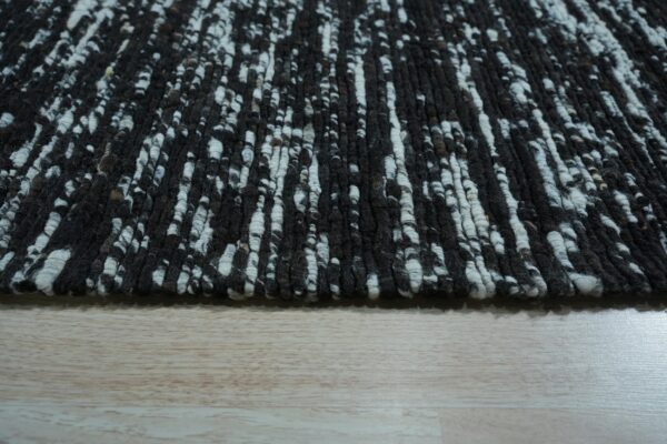 High-pile rug featuring a black and white mottled, vertical texture on light wood planks.