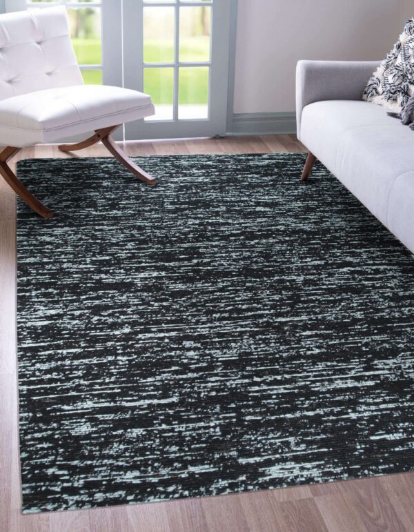 Black and white streaky abstract rug lies beneath a white chair and gray sofa on light wood floors.